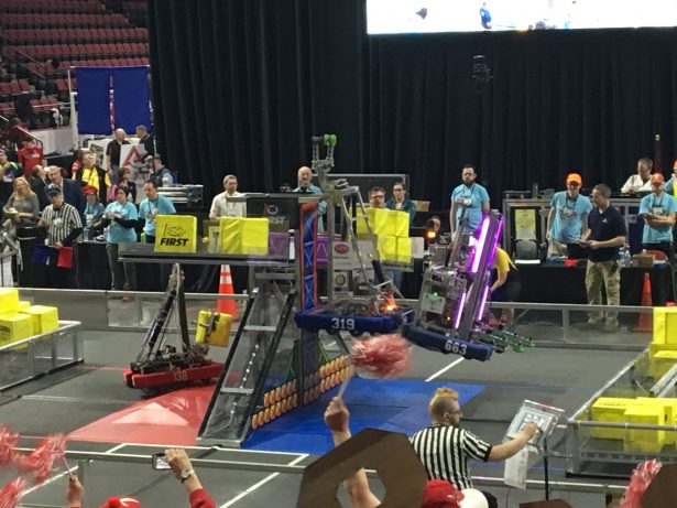 Two bots lift up the POWER UP scale to fight the boss at the FIRST New England District Championship